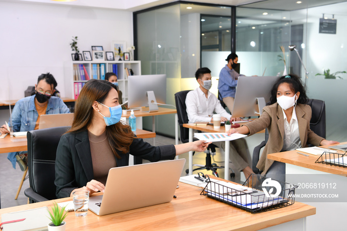 Asian office workers wearing face masks working in new normal office and doing social distancing during corona virus covid-19 pandemic