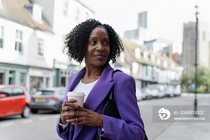 Portrait of smiling woman standing with disposable cup on sidewalk