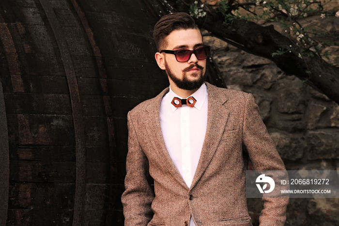 Stylish and brutal young man in a jacket with a beard and a tie looks out to the side