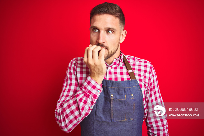 Young handsome man wearing shop owner apron uniform over red isolated background looking stressed and nervous with hands on mouth biting nails. Anxiety problem.