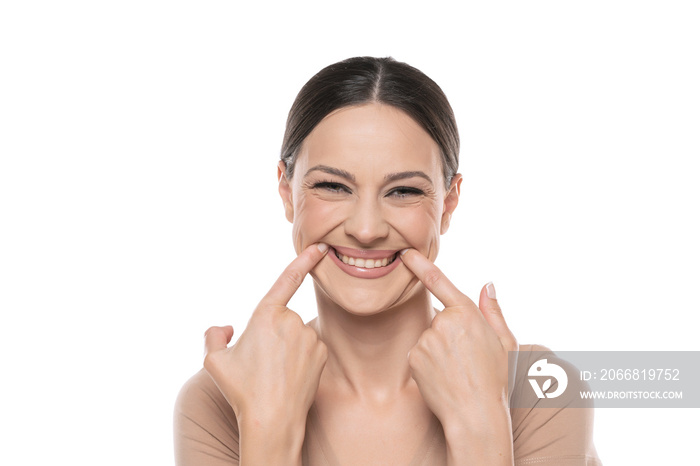 Young beautiful brunette woman wearing casual shirt standing over white background Smiling with open mouth, fingers pointing and forcing cheerful smile