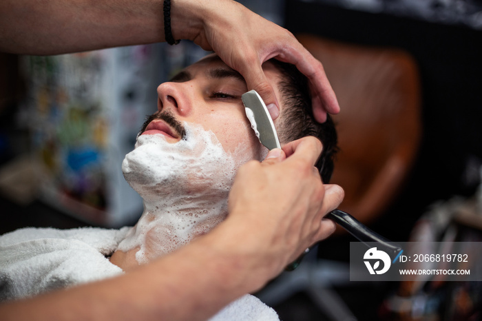 Razor in hands of specialist barber. Barber shaving a man in a barber shop, close-up. Man mith mustaches having a shave