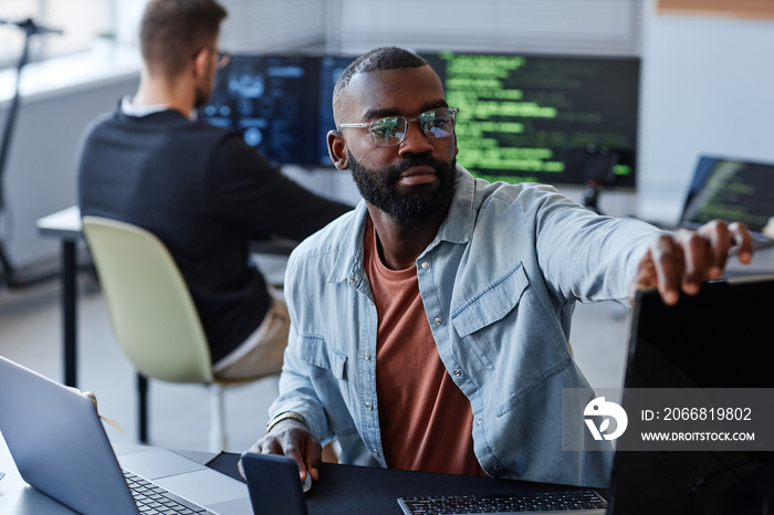 Portrait of black man adjusting computer screens while writing software code in office