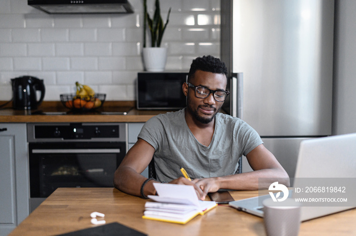 African american male freelancer sitting at the desk, look at the laptop screen. Happy young student taking notes, remotely studying. Successful business man searching ideas, working on project