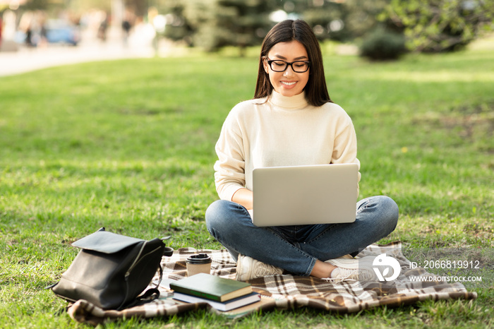 Student in specs using laptop, sitting in the park