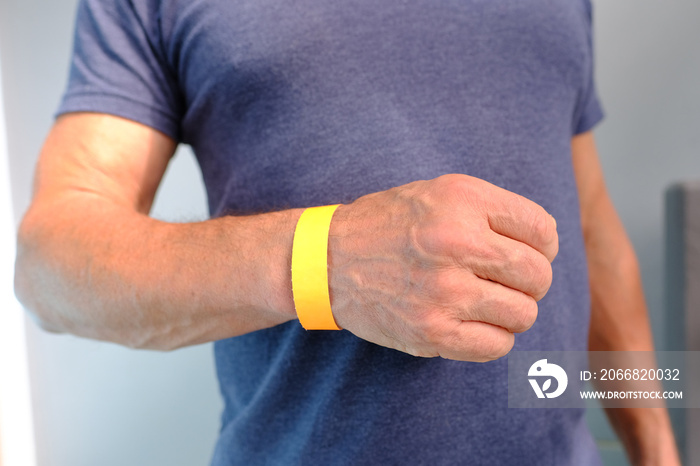 close-up of yellow paper bracelet, check tape with entry number on hand of middle-aged european man, event ticket concept