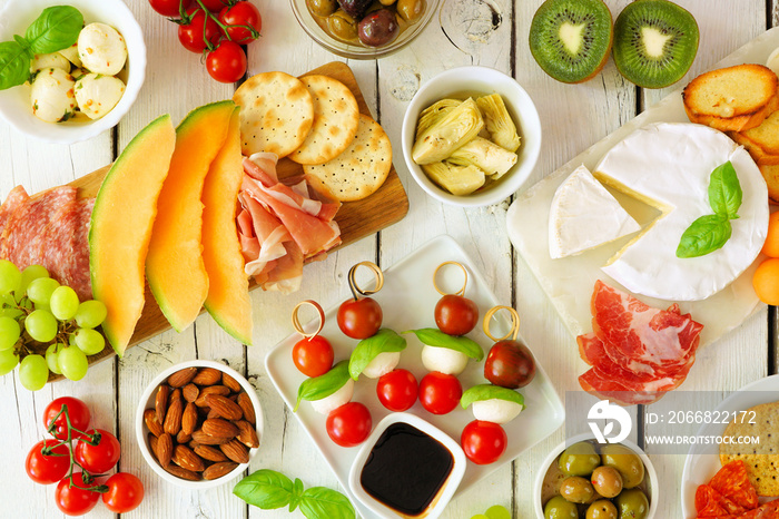 Italian theme grazing table scene against a white wood background. Selection of cheese, meat and fruit appetizers. Overhead view.