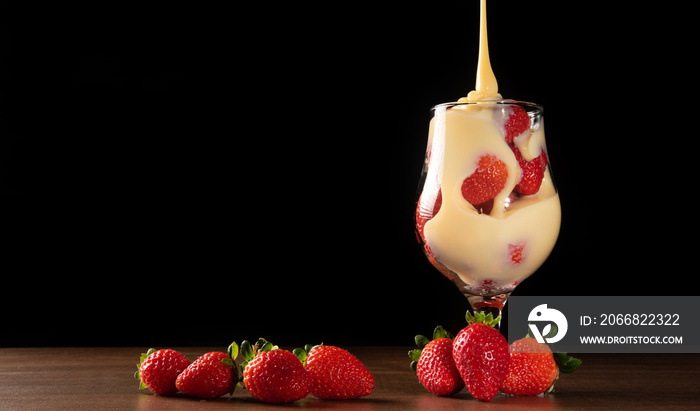 Strawberries, crystal bowl with strawberries and condensed milk on a table, black background, selective focus.