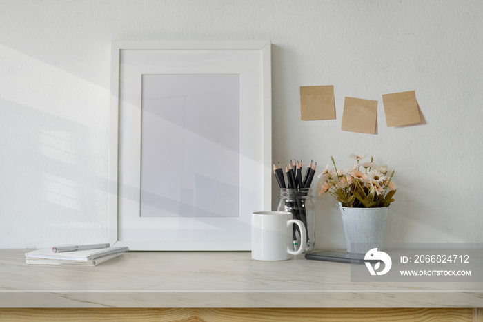 Mockup workspace table with white poster frame, coffee mug, notebook and supplies.