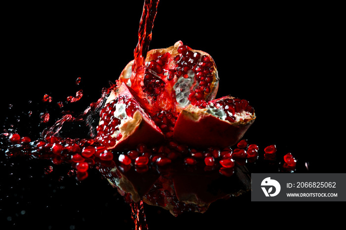 Tasty fresh pomegranate and splashing juice on black background