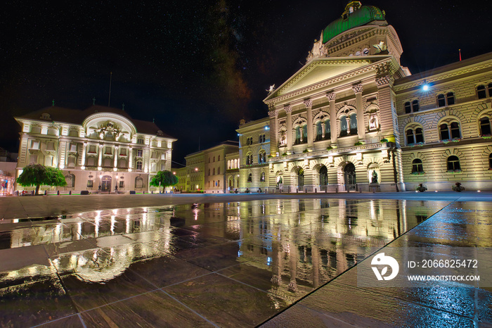 Federal Palace facade in Bern, Switzerland and Swiss National Bank illuminated at night. Swiss Parliament building reflecting in water in Bundesplatzn. Historical old town Bern, Capital of Switzerland