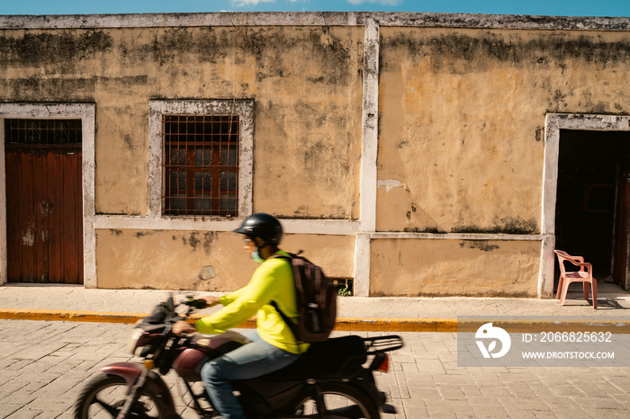 beautiful building beige wall moldy texture shaby. two arched entrances with doors. motobike passing by. streets of a mexican city valladolid