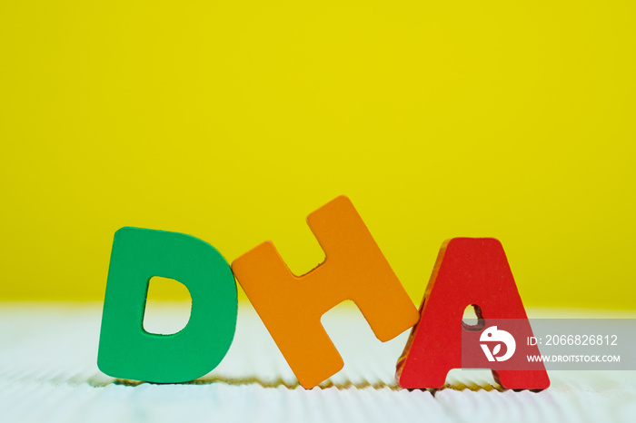 DHA text alphabet on white wooden table. yellow wall background with copy space.