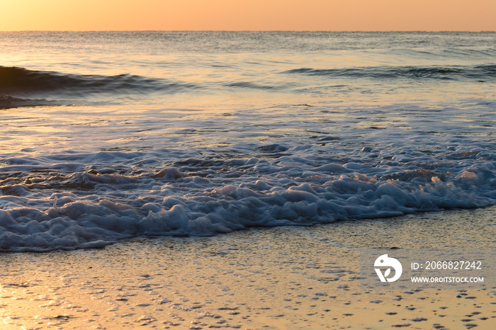 Gentle rolling waves breaking on peaceful empty beach at sunrise