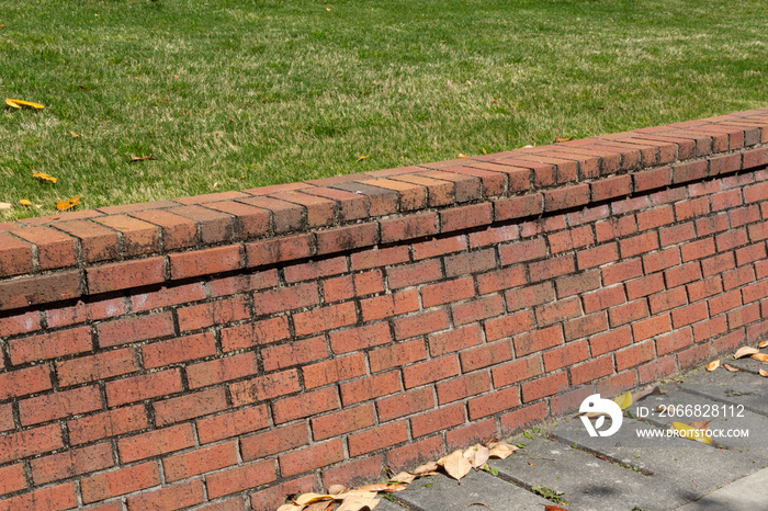 Brick retaining wall with dirt stained mortar, green grass and concrete, horizontal aspect