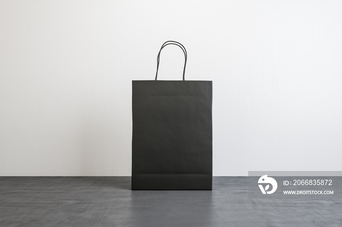 Front view on blank black paper shopping bag with place for your logo or text on concrete floor on white background. 3D rendering, mock up