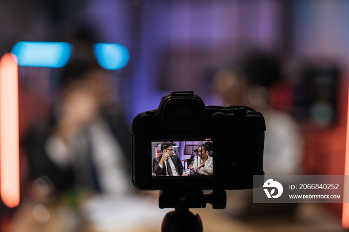 View from camera screen of two confident coworkers indian bearded businessman and african woman broker in headset sitting in front of camera in evening office during recording video for business vlog.