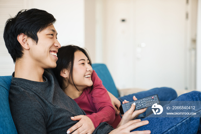 Photo of joyful asian couple watching tv and using remote control