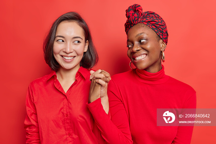 Friendship sign. Happy women shake hands together being best fiends reconcile with each other after quarrel smile gladfully isolated over bright red background wear casual clothing pose indoor