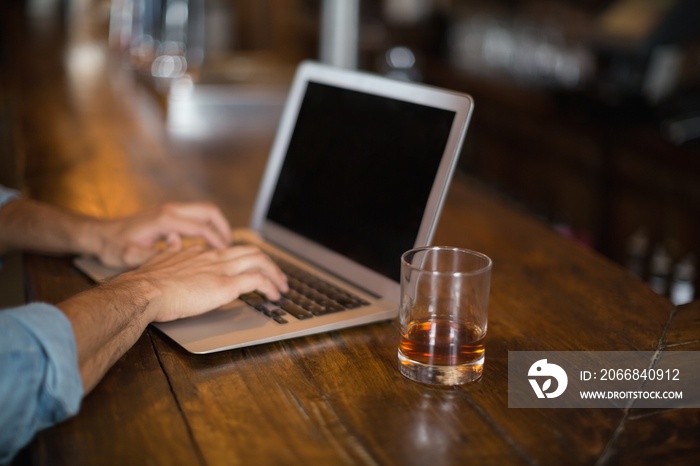 Cropped hands using laptop by beer glass at pub