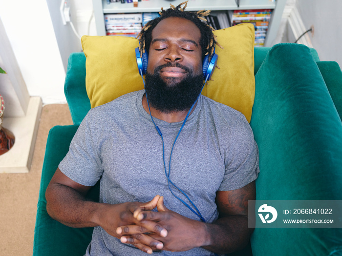 Man lying on sofa, listening to music on headphones