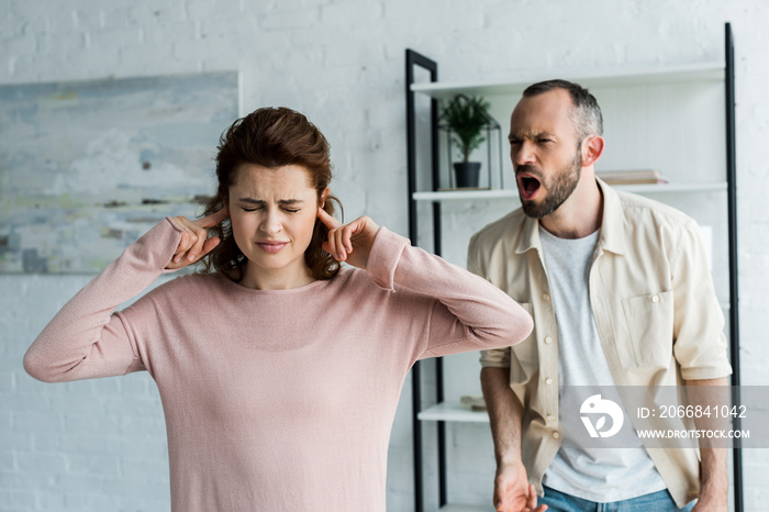 selective focus of woman with closed eyes covering ears near screaming man