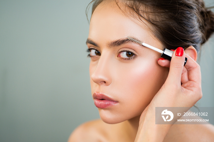 Care eyebrow. Makeup artist applying a brow gel on the eyebrows of a young beautiful woman with flawless nude natural makeup. Concept of professional make up doing.