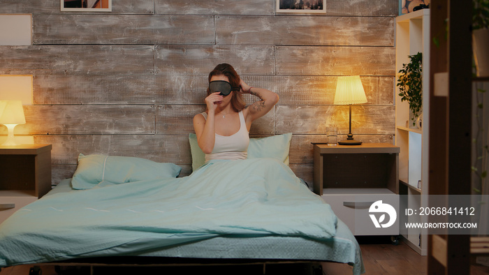 Beautiful woman in pajamas using her phone before going to sleep. Sleep mask.