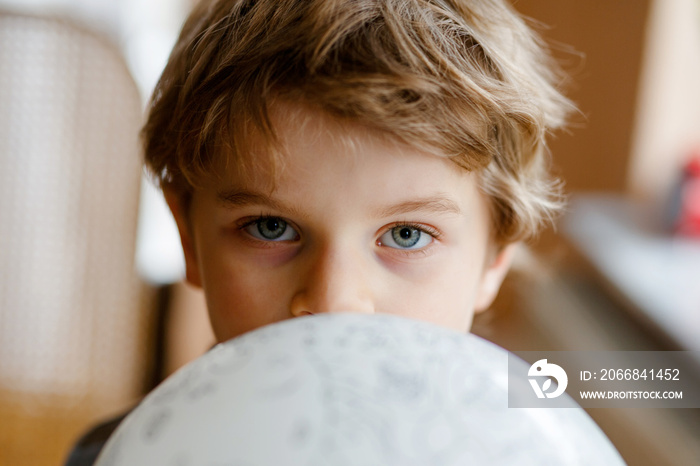 Little blond preschool kid boy with air balloon ball playing indoors at home or nursery. Funny child having fun alone. Happy childhood, kindergarden, school