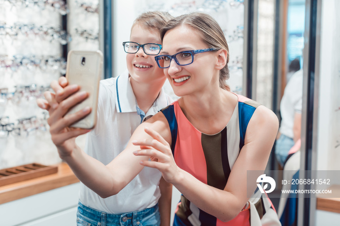 Mother and son taking selfie with new glasses at optometrist shop being happy