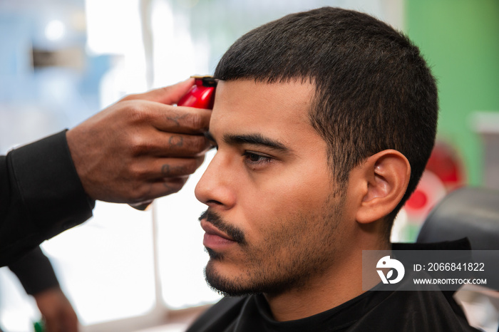 African-American barber’s hand uses razor and haircut on Hispanic Latino man with goatee in a barbershop