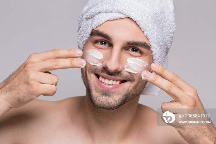 Cheerful man applying moizturizer on his face