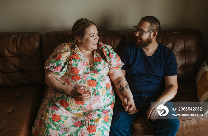 couple sits on couch holding hands chatting