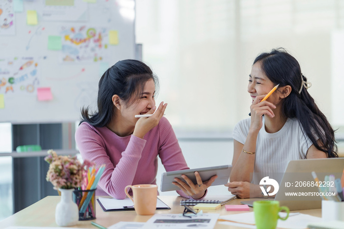 Happy two young Asian business women discuss investment projects and new business planning strategies at the office happily and without stress.