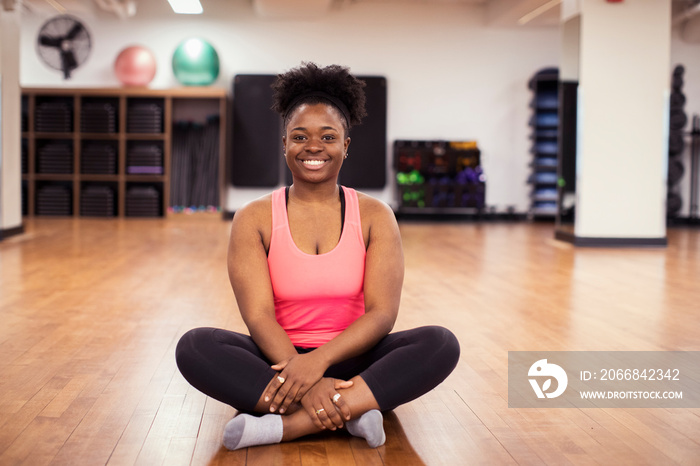 Portrait of happy female athlete sitting on hardwood floor in gym