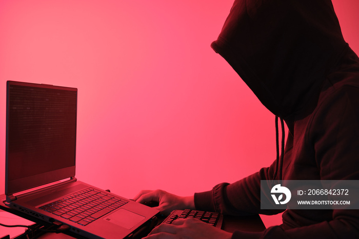 Hooded hacker in front of a computer for organizing massive data breach attack around the world. Cyber criminal concept.