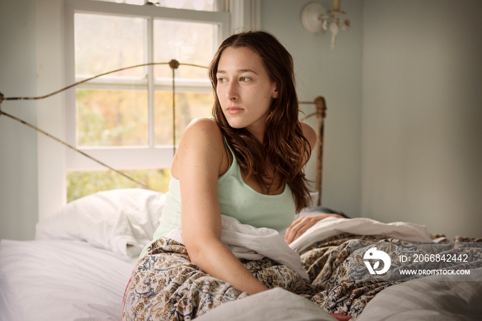 Yong woman sitting in bed and looking away