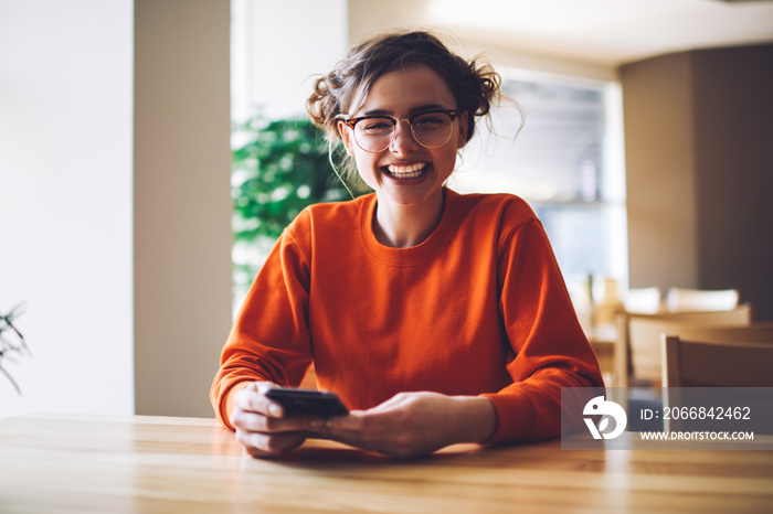 Funny hipster girl feeling happy received good offer on email box sitting in coffee shop during free time, cheerful female student in casual sweatshirt chatting with friend in social networks