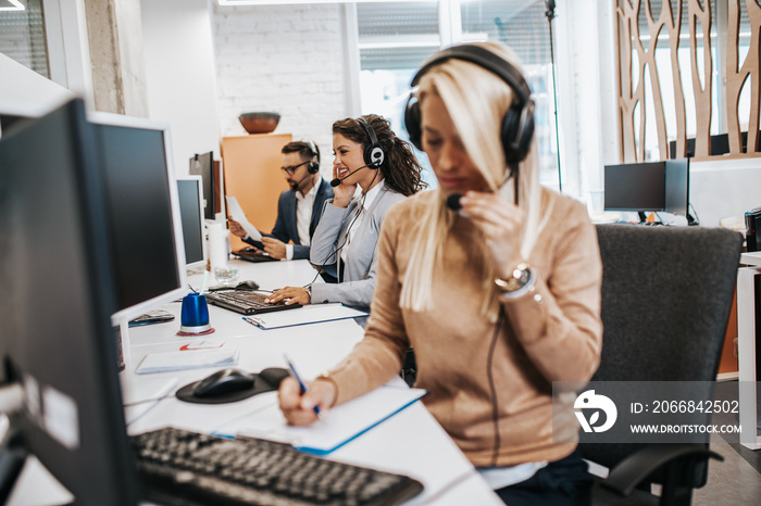 Beautiful smiling female call center worker accompanied by her team working in the office.