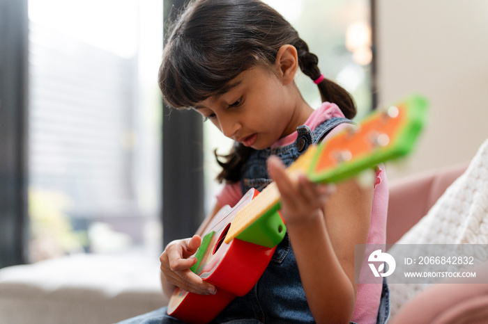 Little girl playing on ukulele in living room