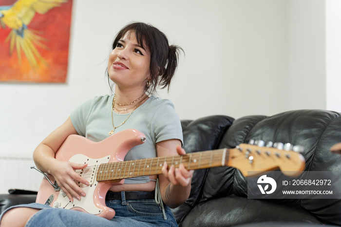 Young woman sitting on sofa and playing guitar