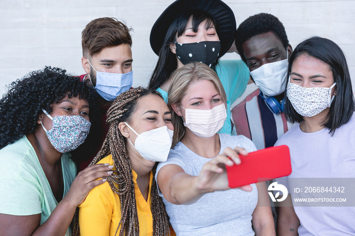 Multiracial young people taking selfie with phone camera while wearing protective masks - Happy friends taking photos during coronavirus outbreak - Social distancing concept - Focus on on girls faces