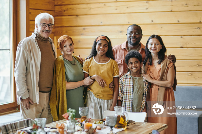 Happy interracial family of three generations standing by served festive table and looking at you with smiles