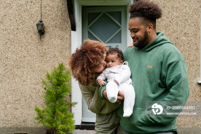 Parents holding baby daughter in front of home