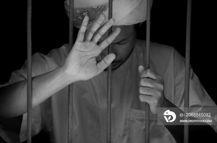Religious muslim islam man in white session hold steel in jail on black background, concept for prisoner,sadness,detain,erroneousness
