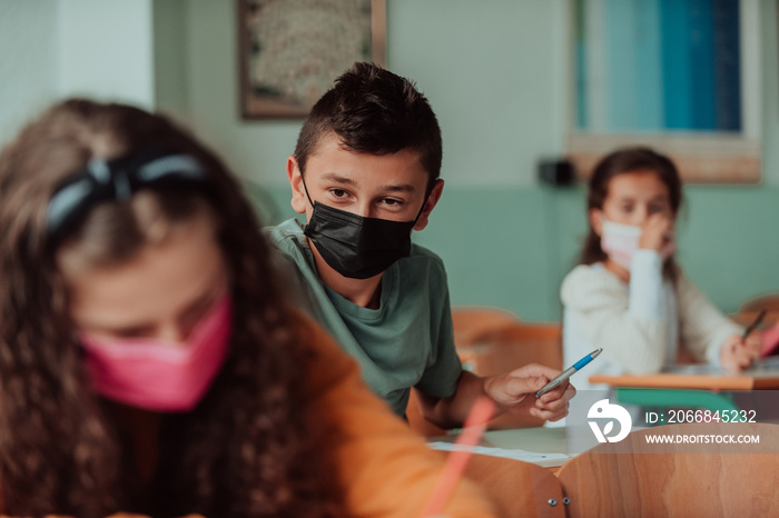 The boy is sitting in a school desk and wearing a mask on his face against corona virus protection. New normal. Education during the Covid-19 pandemic. Selective focus.