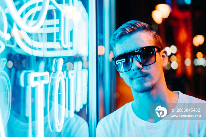 Young Man Wearing Sunglasses at Night in front of Neon Lights