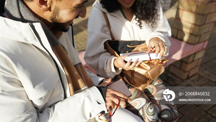 Close-up of couple opening gifts on bench outdoors