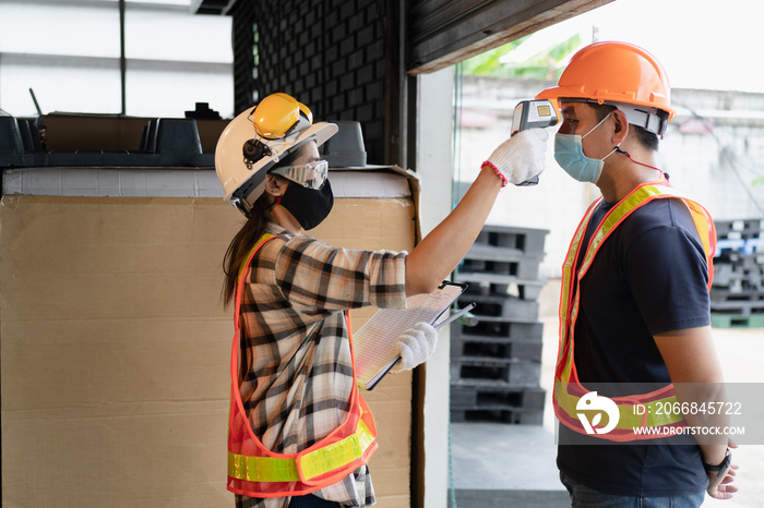 Industrial worker wearing face mask and getting measure temperature for flu scanning by safety inspector before access factory area. New normal workwear after covid-19 pandemic. Covid 19 protection.