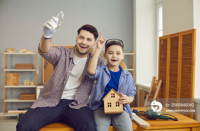 Like father like son portrait. Happy child and dad working on house model project and having fun at carpenter’s workshop. Man teaching little boy to use hand tools and make wooden toys and birdhouses